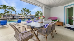 An outdoor patio with a pool, lounge chairs, and a table with a vase of flowers. - 7 Dockside Dream: 3br/3ba Pool Home W/ Water Views! 3 Bedroom Home (Fort Myers Beach)