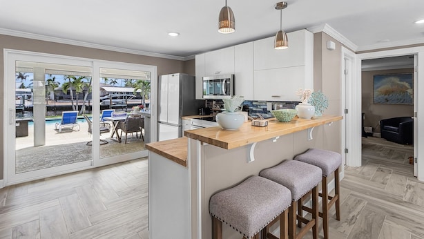 A modern kitchen with a wooden countertop, bar stools, and a view of a pool area. - 7 Dockside Dream: 3br/3ba Pool Home W/ Water Views! 3 Bedroom Home (Fort Myers Beach)
