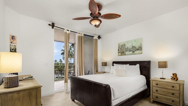 A bedroom with a large bed, a ceiling fan, a nightstand, and a view of the outdoors. - Waterside #835: Bayscape Bliss 3br/2ba Condo W/ Pool! 3 Bedroom Condo (Fort Myers Beach)