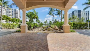 A covered walkway with palm trees and a rocky area in the background. - Waterside #835: Bayscape Bliss 3br/2ba Condo W/ Pool! 3 Bedroom Condo (Fort Myers Beach)