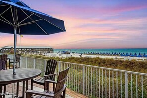 A balcony with a table and chairs, overlooking a beach with umbrellas and lounge chairs.
