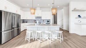 Une cuisine moderne avec des meubles blancs, des appareils en acier inoxydable et un îlot central doté de tabourets de bar.