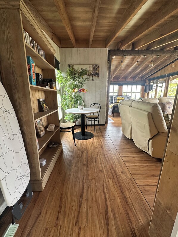 A cozy room with wooden floors, a round table with chairs, a sofa, and a bookshelf filled with books and decorative items. - Riverside wood lodge in Weston, Newark hot tub WiFi wood stove pets parking (Weston)