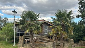 A rustic wooden house with a stone staircase leading to a porch, surrounded by palm trees and a lamp post. - Huge open plan Log Cabin in Weston, Newark hot tub WiFi wood stove pets parking (Weston)