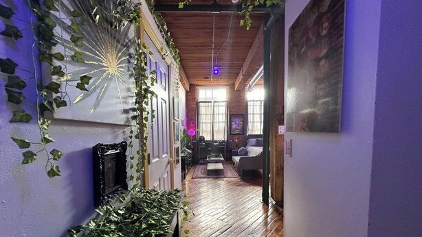 A hallway with wooden flooring, a staircase, and walls adorned with ivy. There is a door at the end of the hallway leading to another room. - Riverside Boho Artist's Loft Downtown (Detroit)