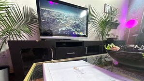 A flat-screen TV on a black entertainment unit, a glass table with a framed welcome sign, and a potted plant. - Riverside Boho Artist's Loft Downtown (Detroit)