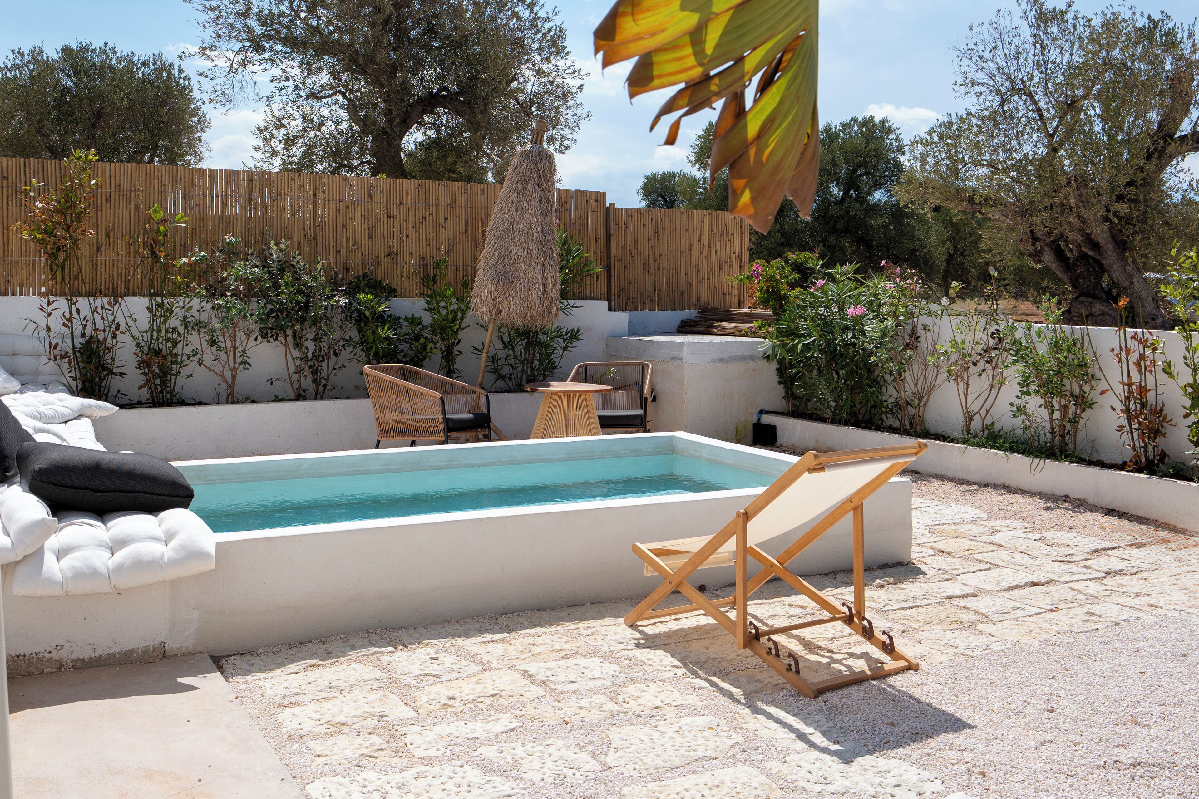 A swimming pool with lounge chairs, a wooden deck, and a bamboo fence.