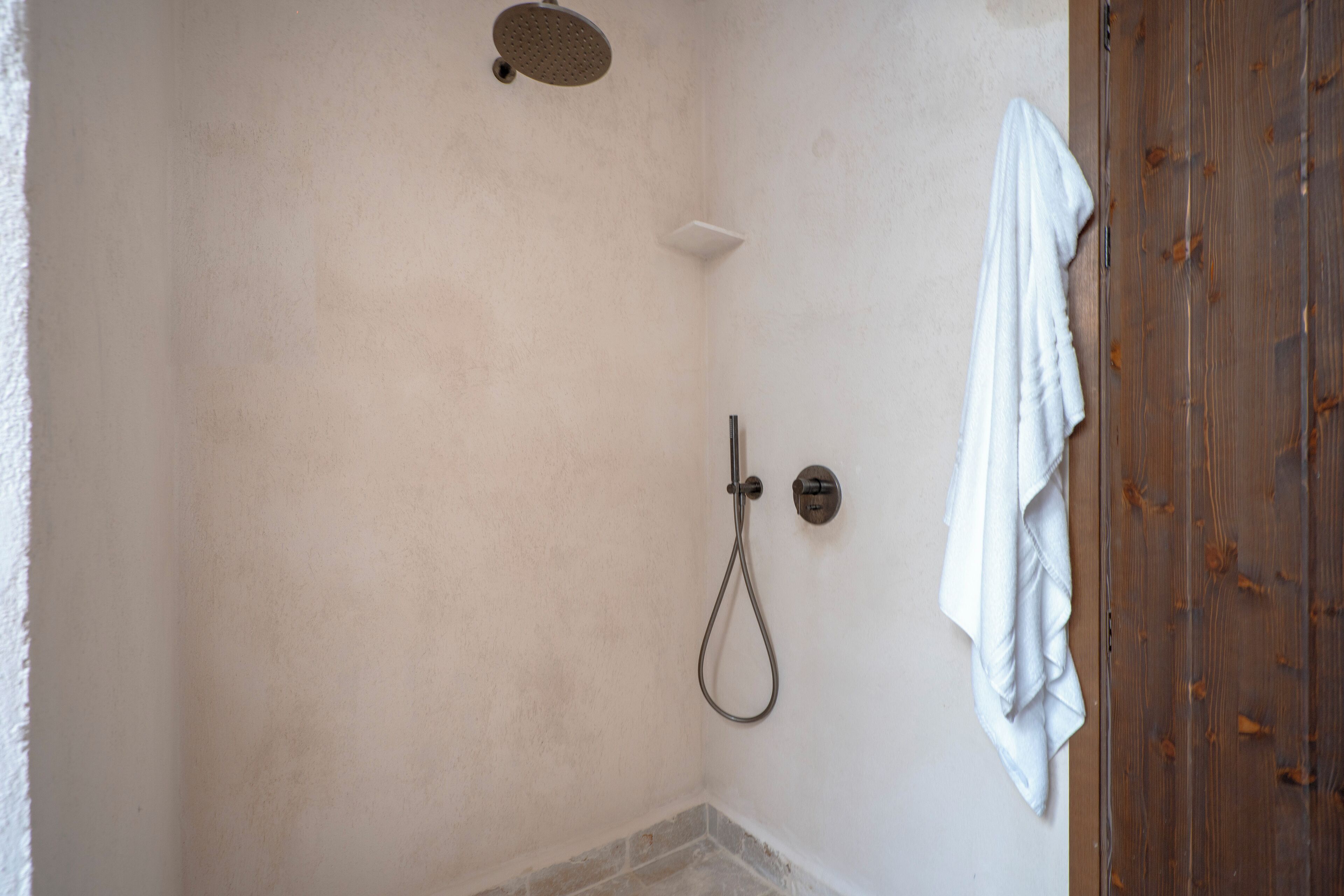 A shower with a handheld showerhead and a wall-mounted control. A white towel hangs on the wall to the right.