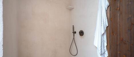 A shower with a handheld showerhead and a wall-mounted control. A white towel hangs on the wall to the right.
