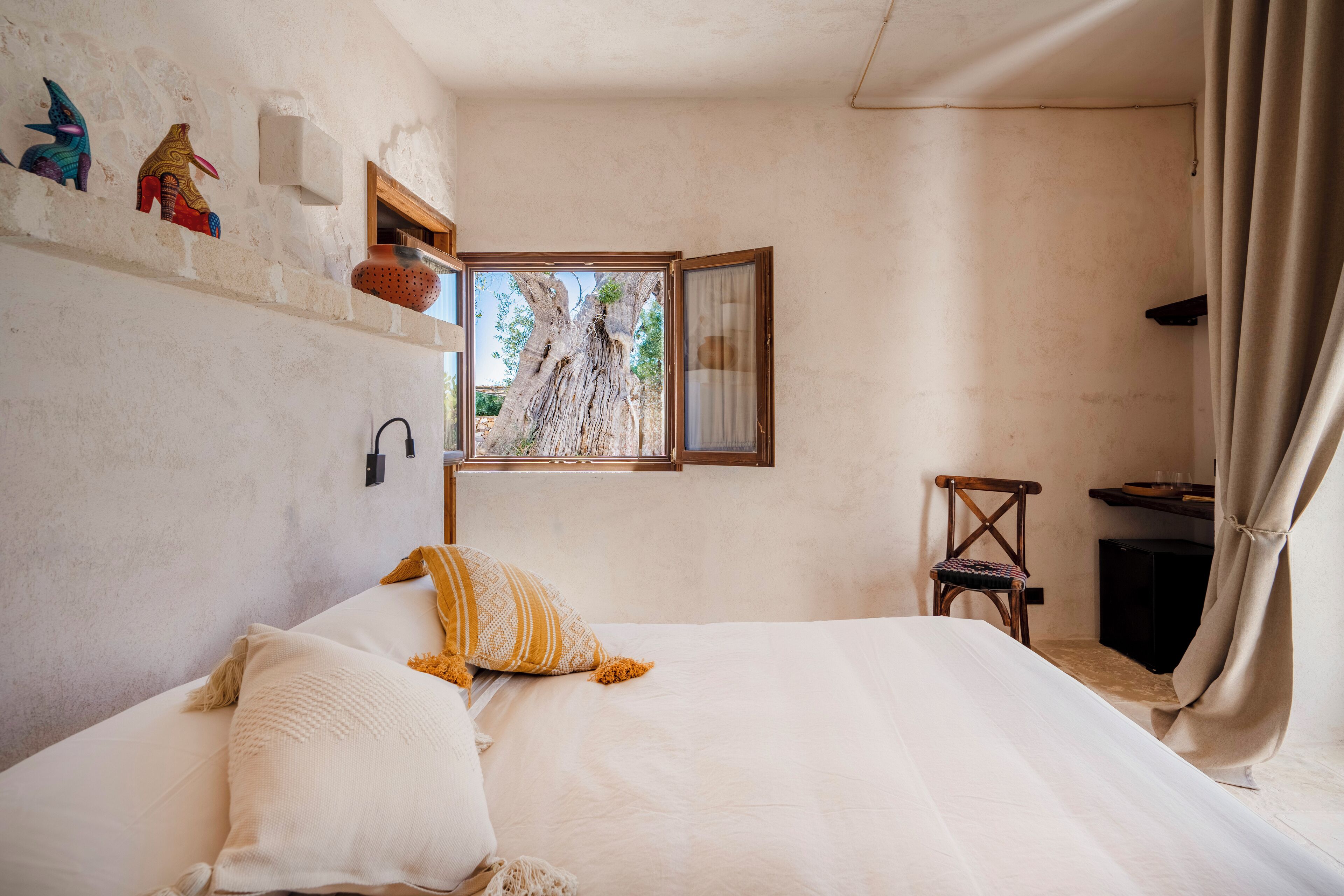 Un dormitorio con cama, ventana, una silla y un estante con objetos decorativos.