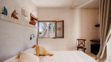 Un dormitorio con cama, ventana, una silla y un estante con objetos decorativos.