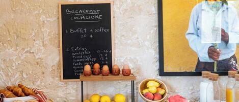 Buffet de café da manhã com cardápio em lousa listando itens como omeletes e sucos naturais.
