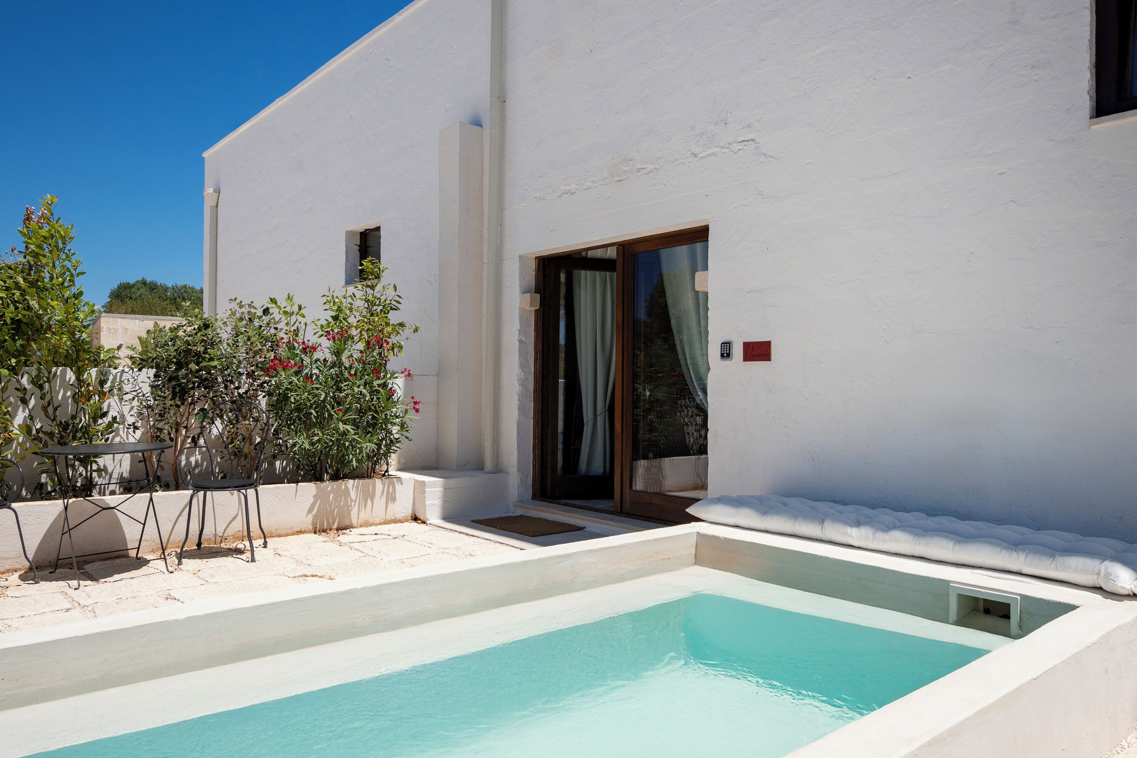 Un edificio moderno con piscina, mobiliario exterior y una puerta con paneles de vidrio.