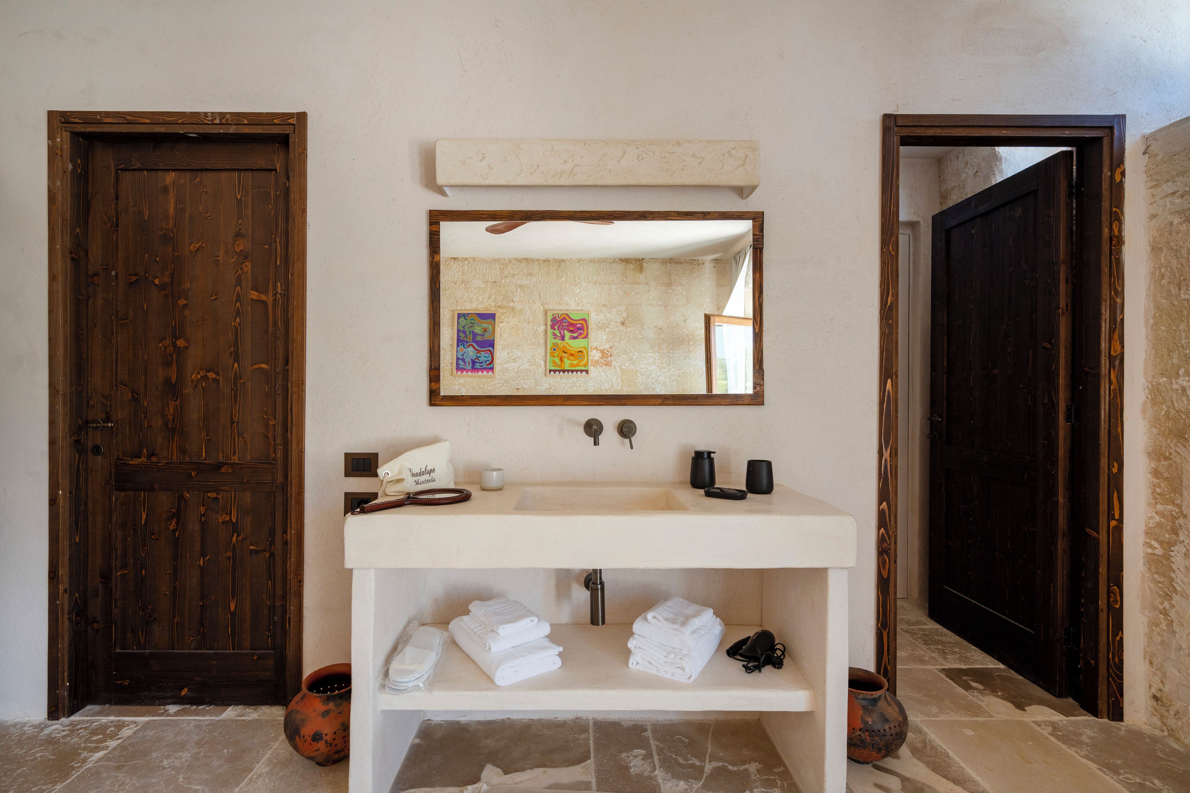 A bathroom with a wooden door, a white sink, and a mirror above it. There are towels and toiletries on the sink counter.