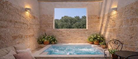 A stone-walled room with a hot tub, a cushioned sofa, and a table with chairs.