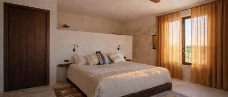 A bedroom with a large bed, a ceiling fan, a wooden door, and a window with curtains.
