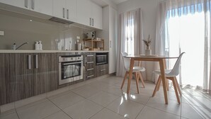 A modern kitchen with white cabinets, a wooden countertop, and a dining area with a table and chairs. - Port Hedland Business Suite - Oceanfront with Fully Equipped Amenities & Wifi (Port Hedland)
