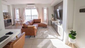 Ein modernes Wohnzimmer mit Sofa, Essbereich, Küche und Fernseher.