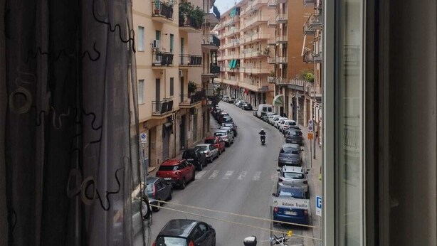 A view from a window overlooking a street lined with parked cars and multi-story buildings.