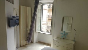 A bedroom with a bed, a dresser, a TV mounted on the wall, and a window with a view of the outside.