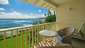 A balcony with a view of the ocean, a round table, wicker chairs, and a railing. - Oceanfront Studio with Panoramic Views - Kapa'a Sands 09 (Kapaa)
