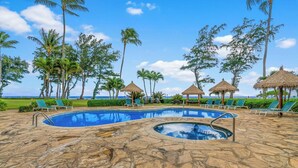 A pool area with lounge chairs and thatched umbrellas, surrounded by palm trees and a view of the ocean.