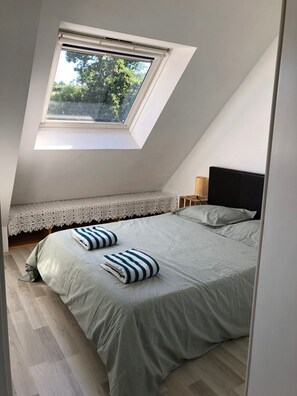 A bedroom with a skylight, a bed with pillows, a bedside table, and a lace-covered bench. - House 100m from Cap Coz beach (Fouesnant)
