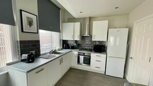 Una cocina moderna con armarios blancos, horno empotrado, estufa y refrigerador.