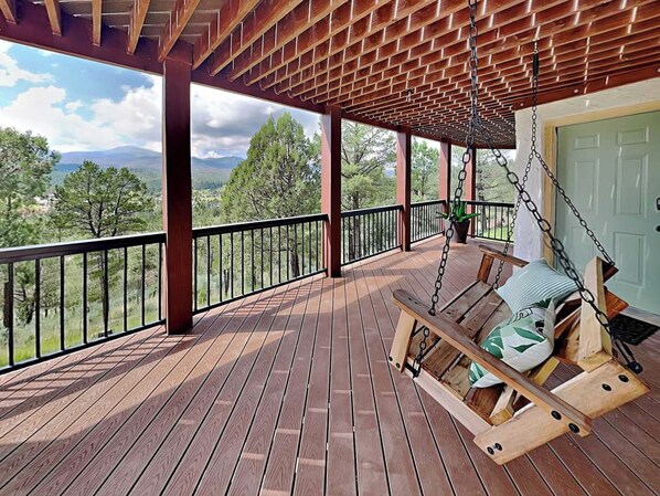 Eine Holzterrasse mit Schaukelstuhl und Blick auf eine gebirgige Landschaft.