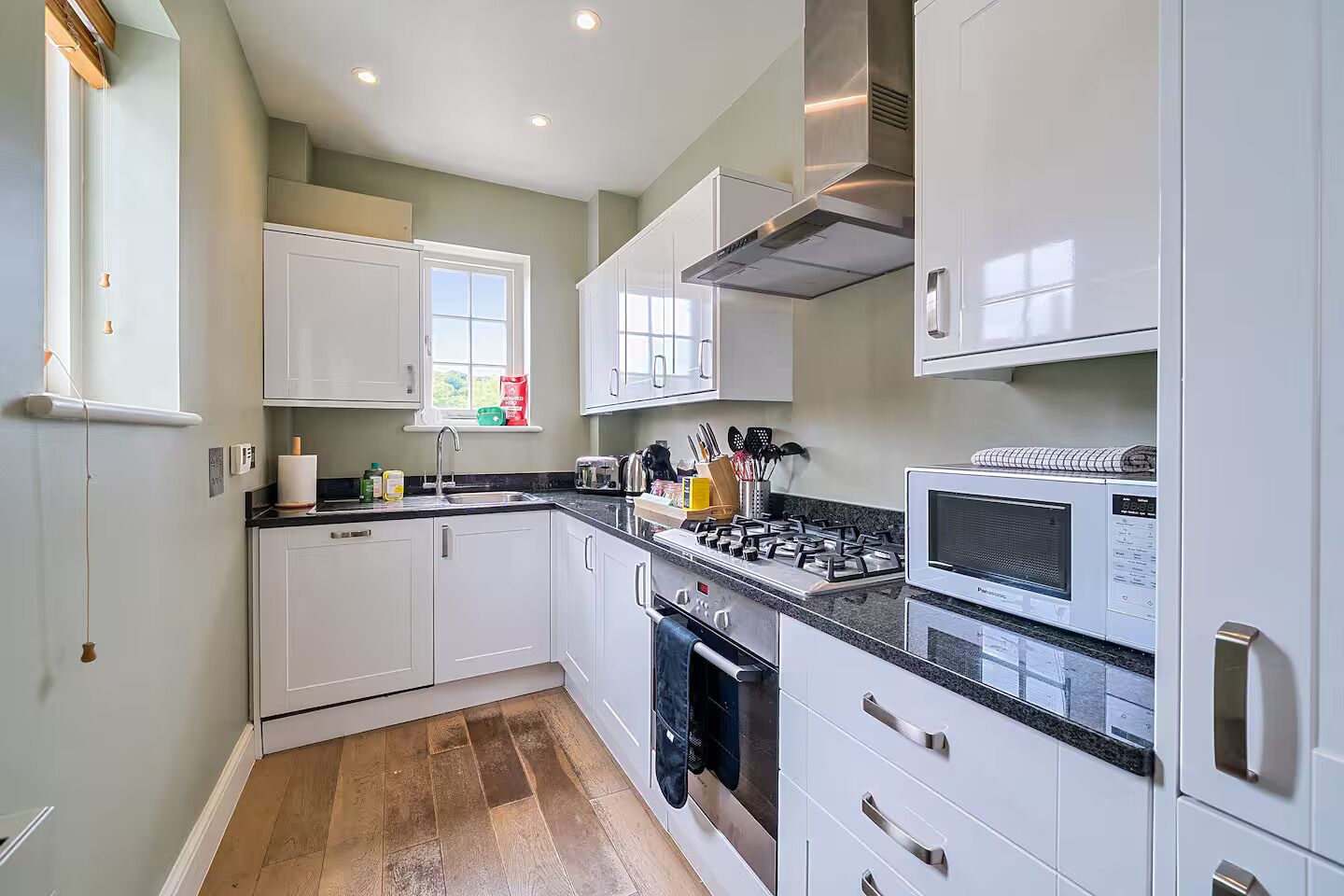Une cuisine moderne avec des meubles blancs, une cuisinière à gaz, un four à micro-ondes et une fenêtre donnant sur un paysage verdoyant.