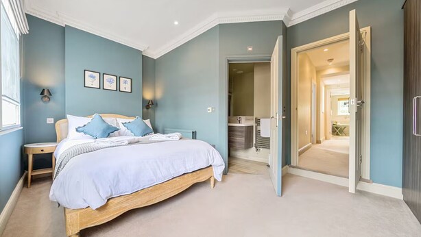 Ein Schlafzimmer mit einem großen Bett, Nachttischen und einem durchgehenden Türrahmen einsehbaren Badezimmer.