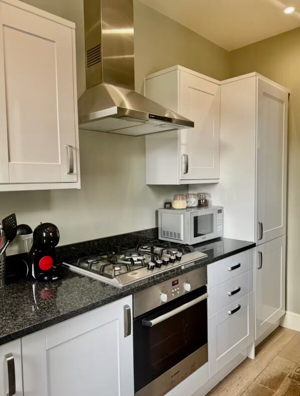 A modern kitchen with white cabinets, a gas stove, a microwave, and a stainless steel range hood.