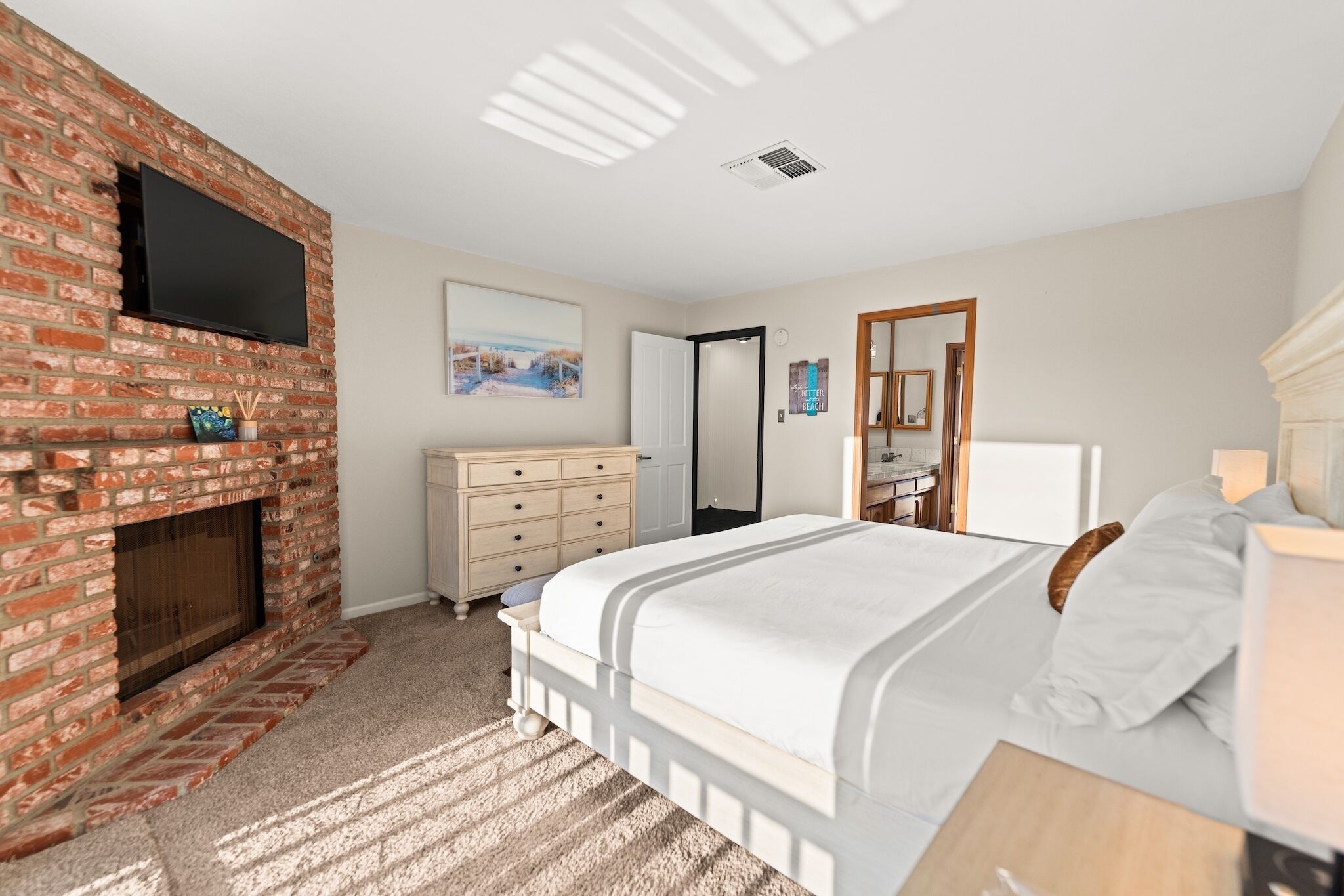 A bedroom with a brick fireplace, a bed, a dresser, and a television mounted on the wall.
