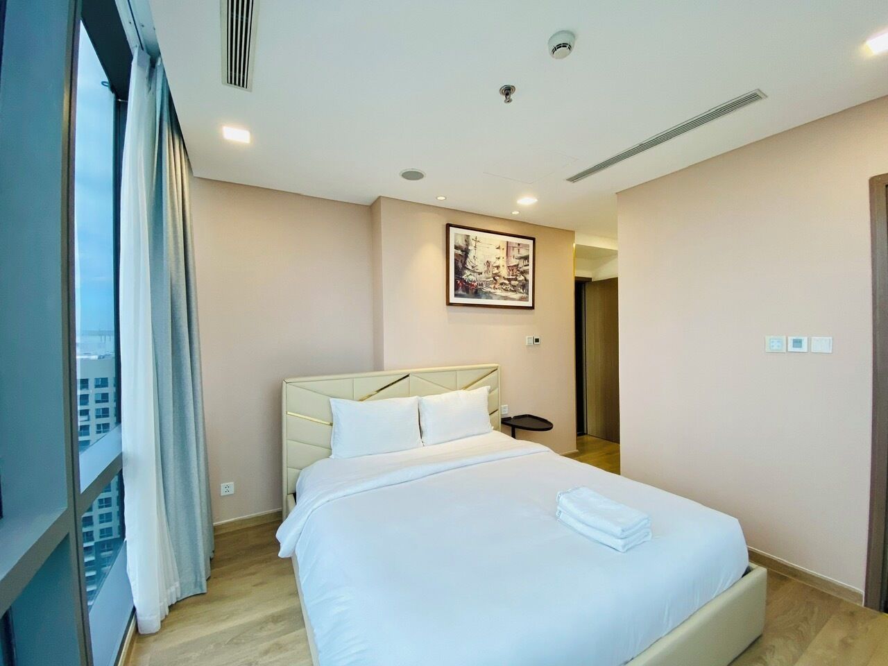 A hotel room with a large bed, a headboard, a bedside table, and a window with curtains.