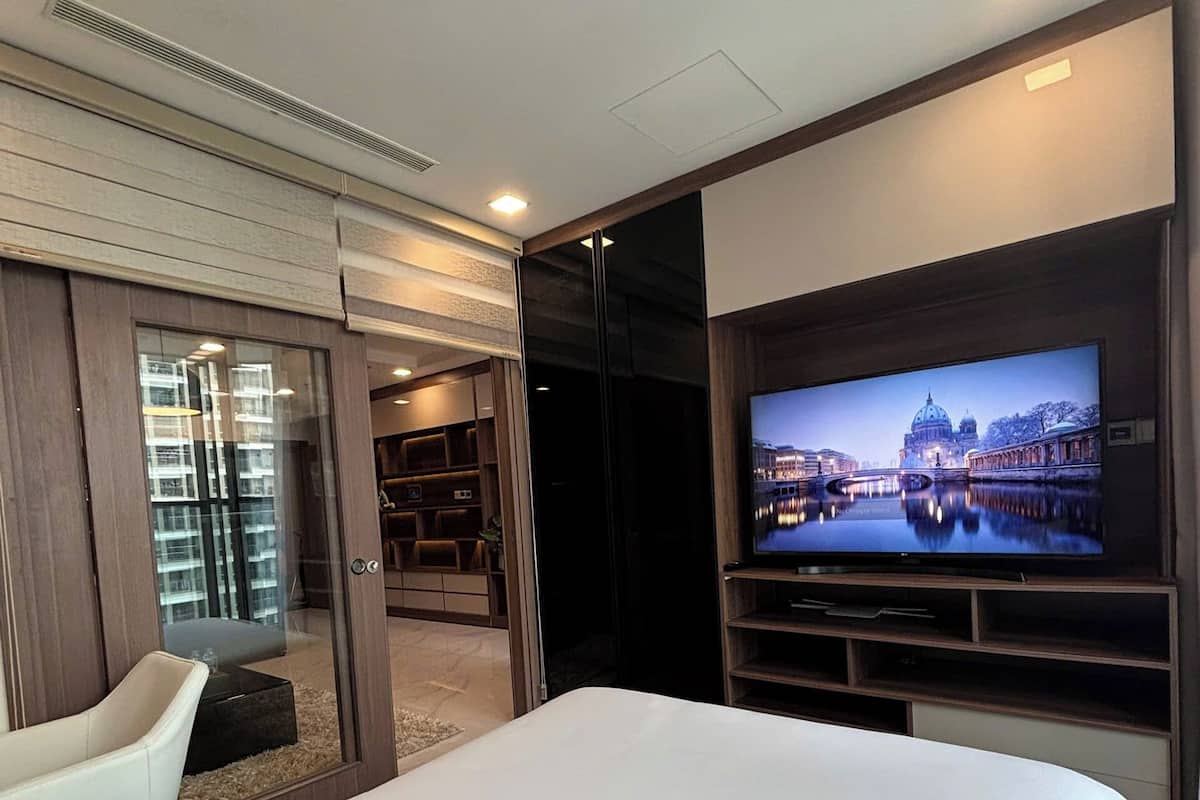 A modern hotel room with a large bed, a television mounted on the wall, and a view of a cityscape.