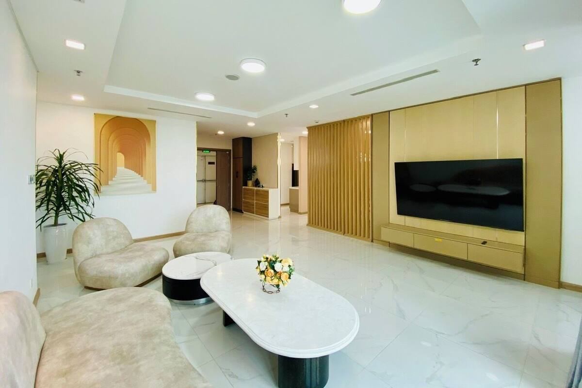 A modern living room with a flat-screen TV, beige sofas, a coffee table, and a potted plant.