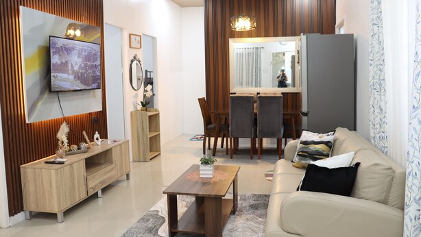 A modern living room with a flat-screen TV, wooden entertainment unit, a sofa, a coffee table, and a dining area with chairs and a table. - Efas Guesthouse Tagum City (Tagum)