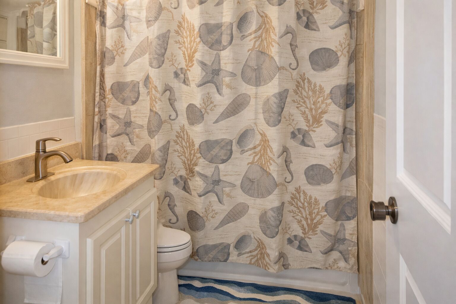 Un baño con lavabo, inodoro y cortina de ducha con motivos marinos.