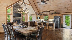 A spacious wooden cabin with a large dining table, multiple chairs, a fireplace, a kitchen area, and a ceiling fan. - Deerly Blissed, Blue Ridge (Blue Ridge)