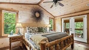 A wooden cabin bedroom with a bed, nightstands, a ceiling fan, and large windows. - Deerly Blissed, Blue Ridge (Blue Ridge)