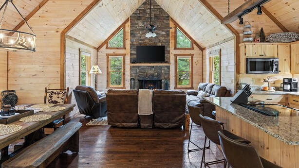 A log cabin interior with a stone fireplace, wooden furniture, and a kitchen area. - Deerly Blissed, Blue Ridge (Blue Ridge)