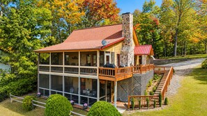 A two-story log cabin with a stone chimney, a deck, and a covered outdoor seating area.