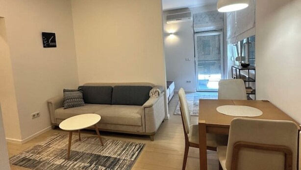 A modern living room with a sofa, a small round table, and a dining area with chairs. - BASC Modern 2 (Sarajevo)