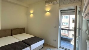 A room with two beds, a ceiling light, an air conditioning unit, and a view of the outside through a door. - BASC Modern 2 (Sarajevo)