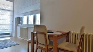 A dining area with a wooden table and chairs, a radiator, and a window with blinds. - BASC Modern 2 (Sarajevo)