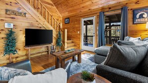 A cabin interior with a wooden staircase, a flat-screen TV, a sofa, and a coffee table.
