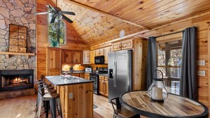 A cozy cabin-style kitchen with a stone fireplace, wooden cabinets, a large island, and a dining area.
