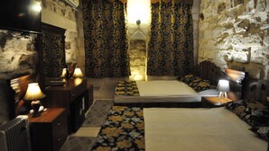 Habitació amb paret de pedra, llit amb estriatges i taula de nit amb làmpada, i cortines amb disseny floral.