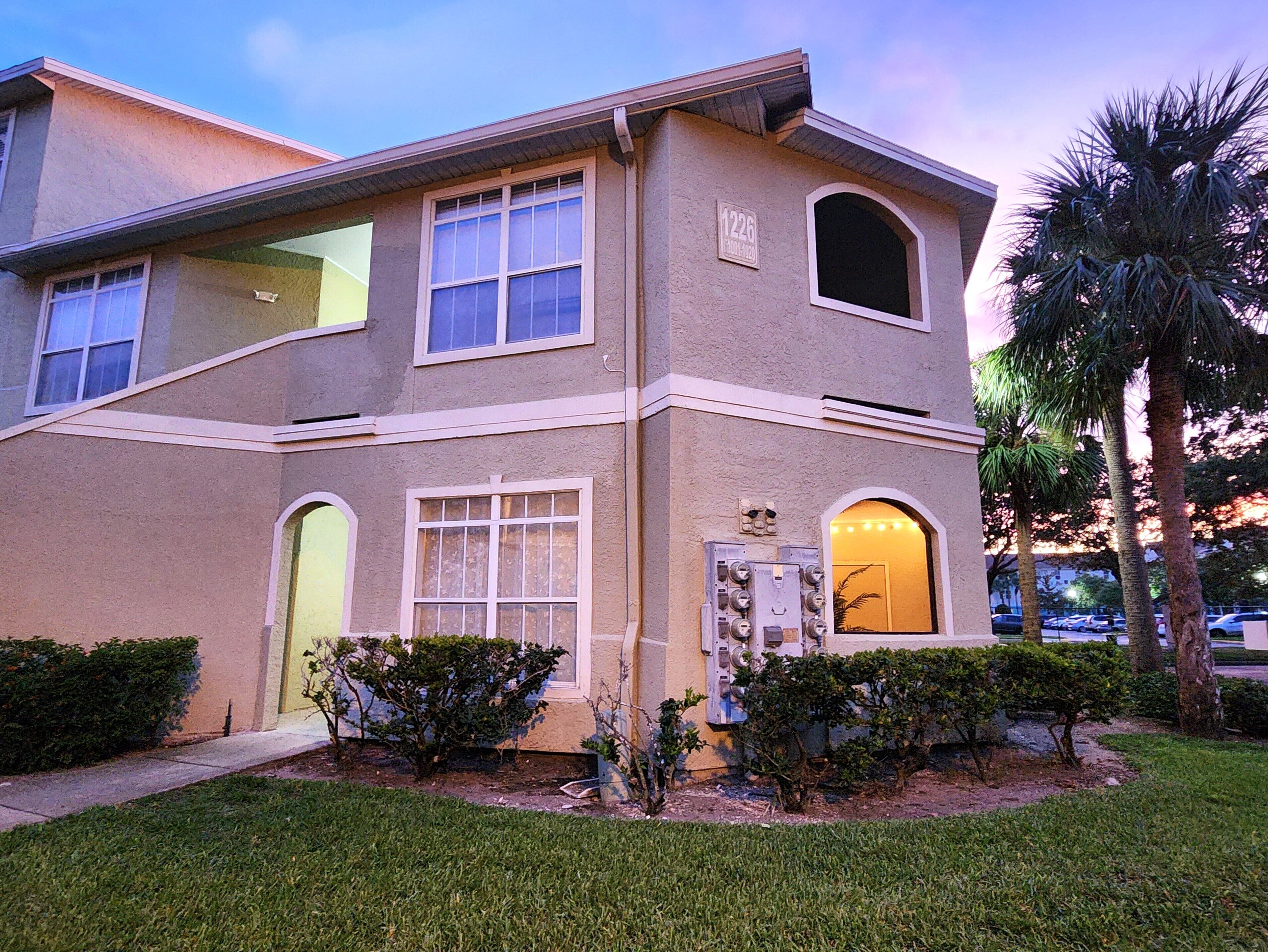 A two-story building with a beige facade, multiple windows, and a small front yard with landscaping.