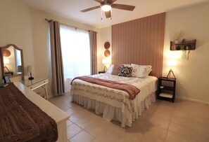 Une chambre à coucher comprenant un lit, des tables de chevet, un ventilateur de plafond, un miroir et une étagère murale décorative.
